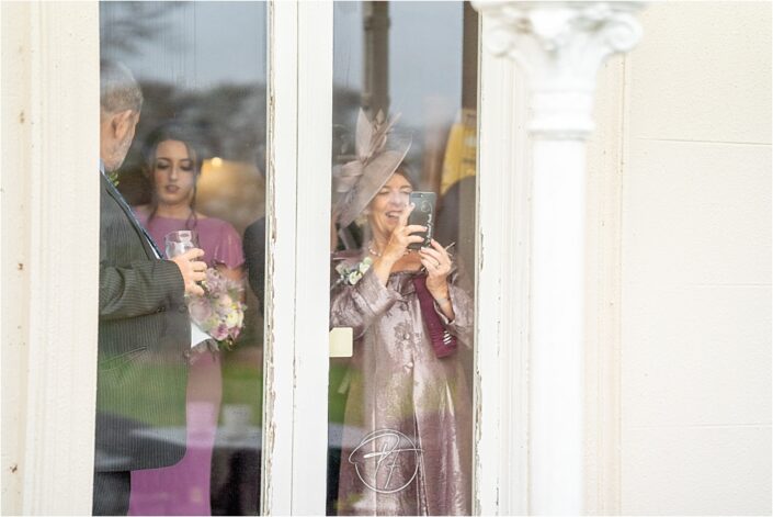 Guests behind glass window take photos of bride and groom